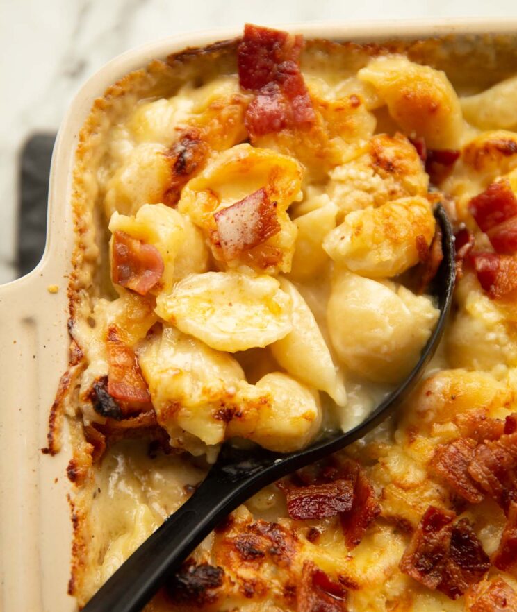 close up shot of cauliflower cheese pasta bake with black serving spoon digging in