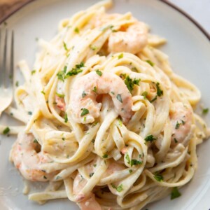 close up shot of creamy prawn linguine on small white plate with silver fork on the side