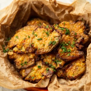 close up shot of parmesan smashed potatoes in scrunched up parchment paper garnished with parsley