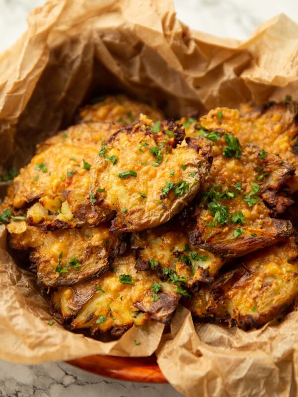 close up shot of parmesan smashed potatoes in scrunched up parchment paper garnished with parsley