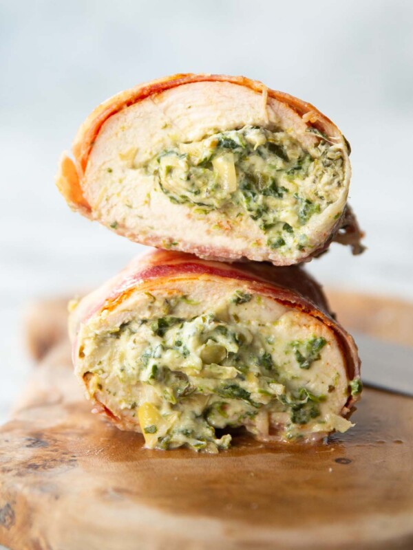 close up side shot showing spinach and artichoke filling inside chicken breasts wrapped in bacon on chopping board