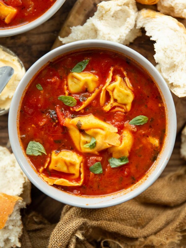 overhead shot of tomato tortellini soup in bowl surrounded by chunks of bread