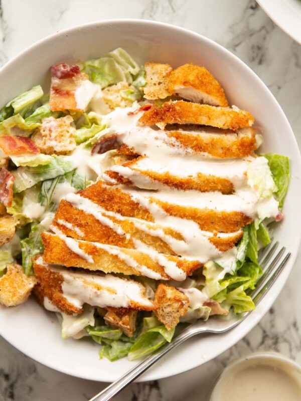 overhead shot of chicken caesar salad in large white bowl on marble backdrop with silver fork