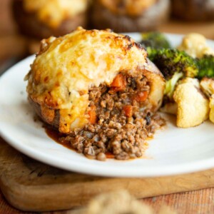 cottage pie loaded potato sliced in half on small white plate with roasted broccoli and cauliflower