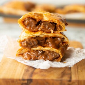 3 Greggs steak bakes stacked on each other on wooden chopping board