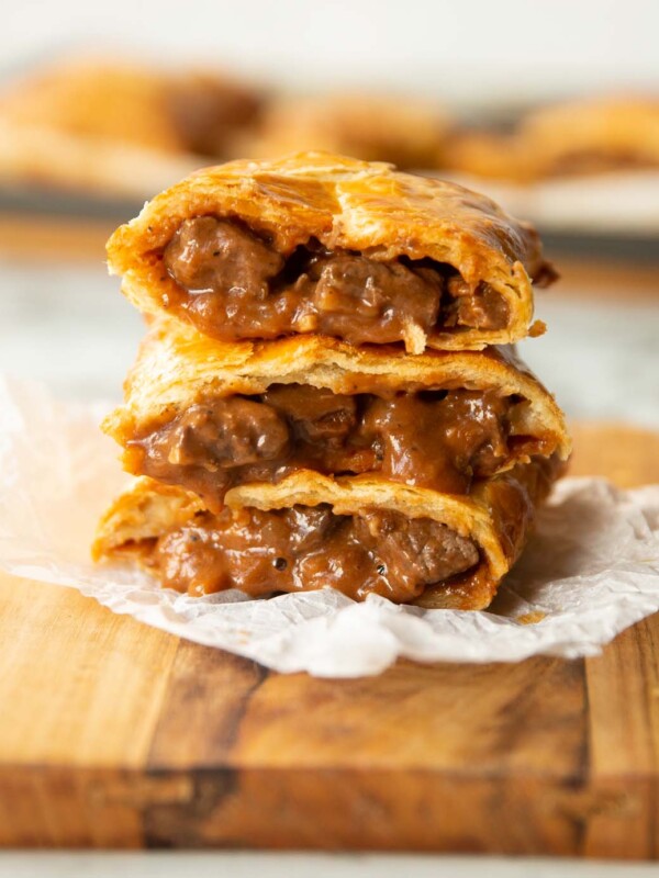 3 Greggs steak bakes stacked on each other on wooden chopping board