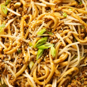 close up shot of spicy pork noodles in pan garnished with spring onion