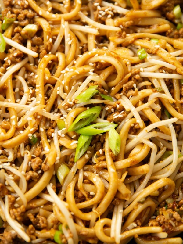 close up shot of spicy pork noodles in pan garnished with spring onion