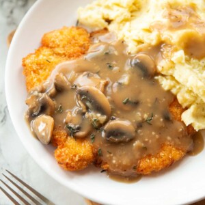 close up shot of chicken schnitzel with mushroom gravy and mashed potatoes on white plate