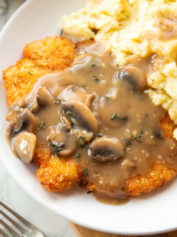 close up shot of chicken schnitzel with mushroom gravy and mashed potatoes on white plate