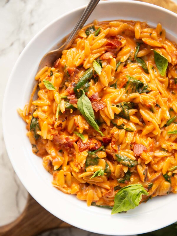 overhead shot of tomato spinach bacon orzo in large whit bowl with silver fork