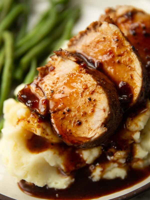 close up shot of sliced cajun pork tenderloin on mashed potatoes with green beans