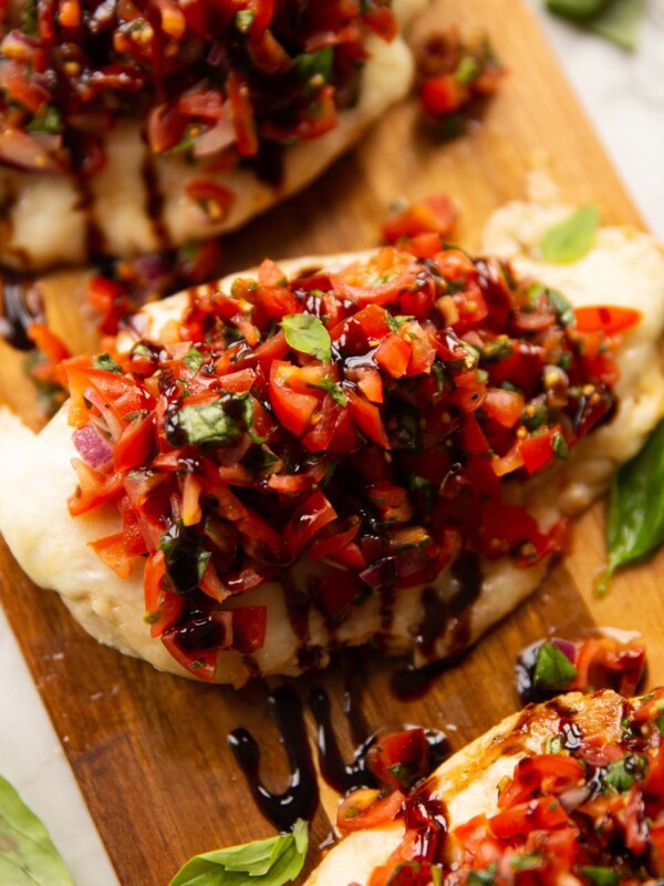 close up shot of chicken bruschetta on wooden board with fresh basil as garnish