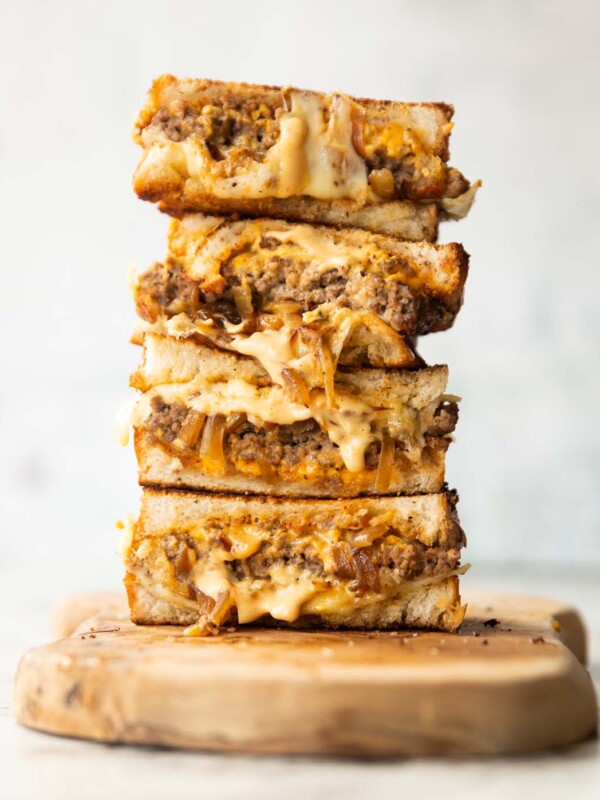 4 patty melt halves stacked on each other on wooden chopping board