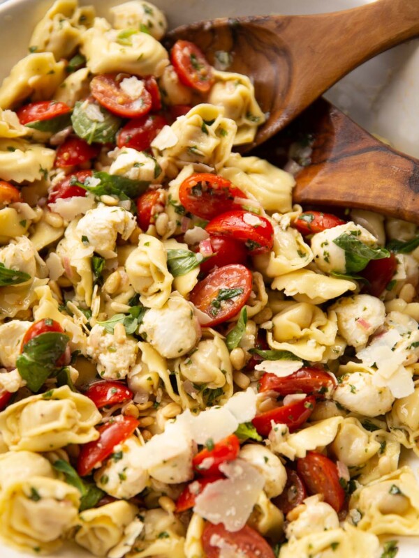 tortellini pasta salad in large white bowl with salad tossers at the back