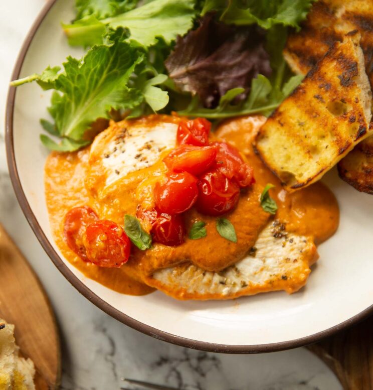 chicken in creamy tomato sauce on small white plate with garlic bread and salad