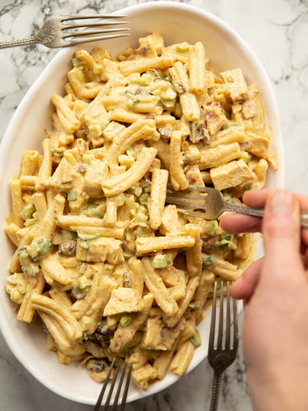 overhead shot of coronation chicken and bacon pasta salad in large oval dish with forks surrounding