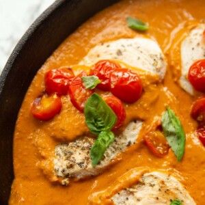 close up shot of creamy tomato chicken in pan garnished with basil