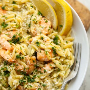 close up shot of garlic butter orzo in large white plate with silver fork