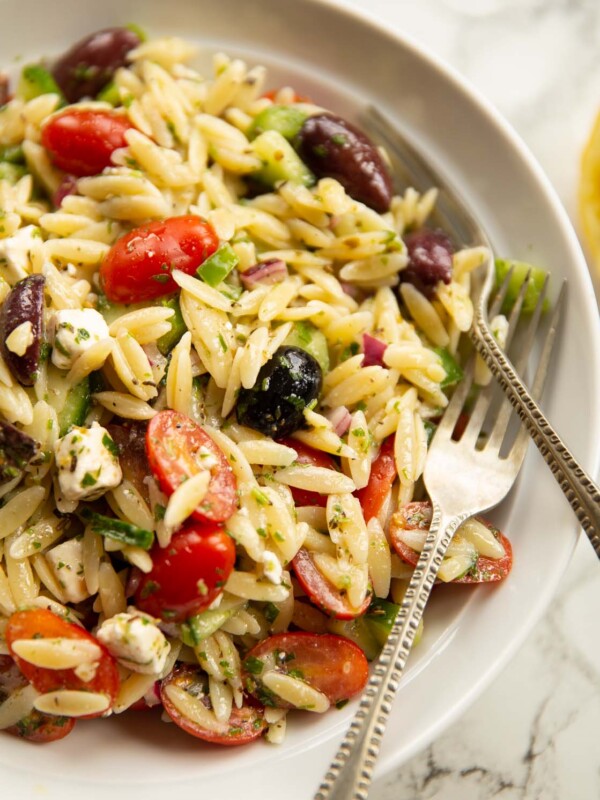 close up shot of greek orzo pasta salad in white bowl with 2 silver forks