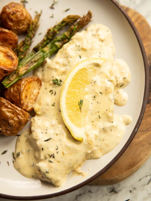 close up shot of lemon thyme pork chop on small white plate with potatoes and asparagus