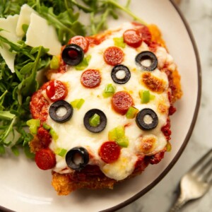 close up shot of pizza chicken parmesan on small white plate with rocket salad