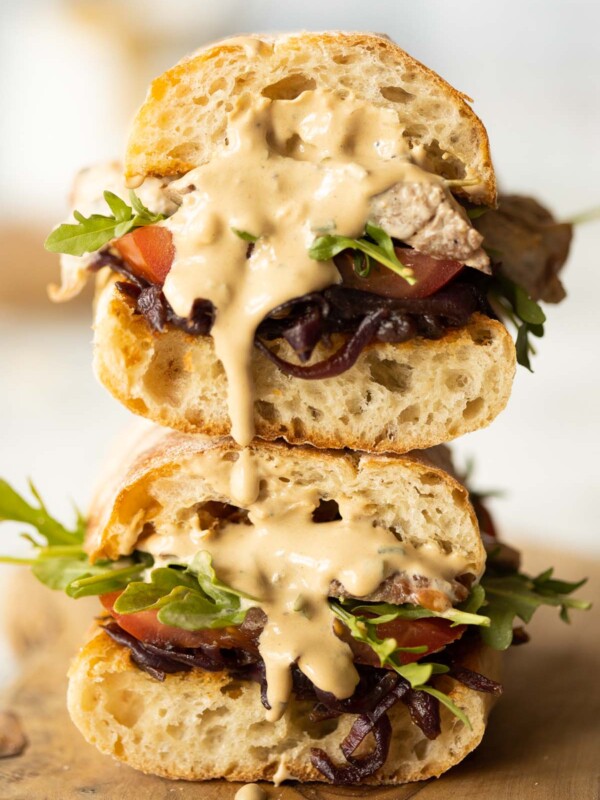 two steak sandwiches stacked on each other with sauce dripping out