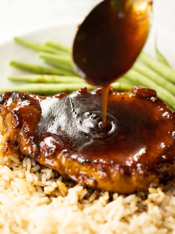 spoon drizzling brown sugar glaze over pork chop on white plate with rice and green beans