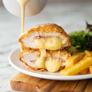 2 chicken cordon bleu halves stacked on each other with small jug pouring sauce over them