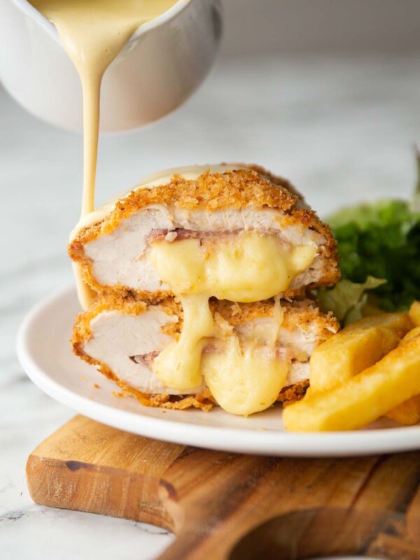 2 chicken cordon bleu halves stacked on each other with small jug pouring sauce over them