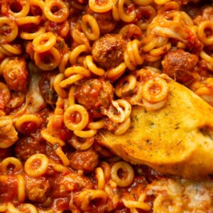 close up overhead shot of garlic bread dunking into pan of spaghetti hoops