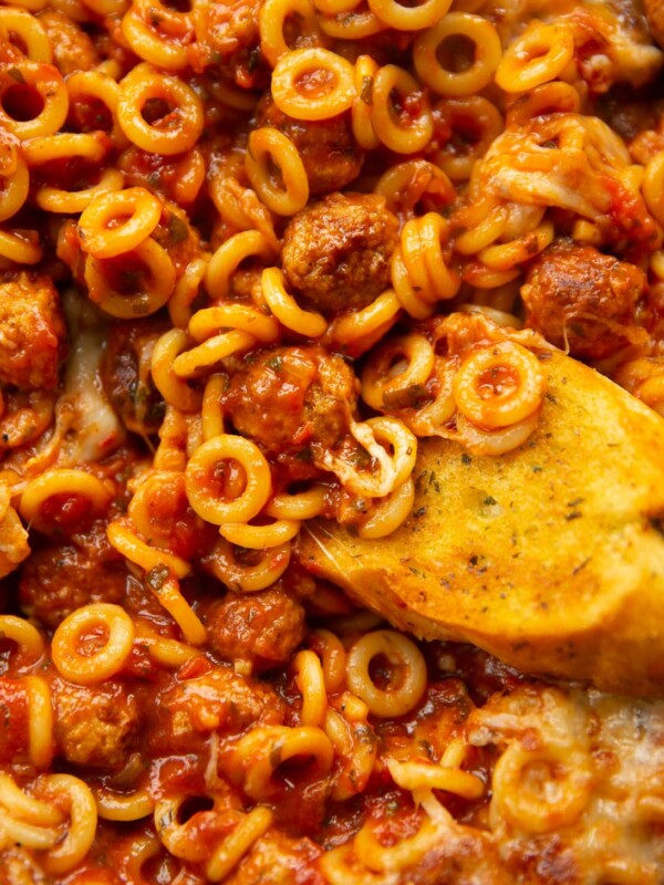 close up overhead shot of garlic bread dunking into pan of spaghetti hoops