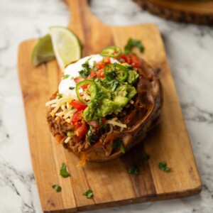 taco stuffed sweet potato on wooden chopping board with limes in background