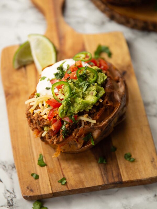 taco stuffed sweet potato on wooden chopping board with limes in background