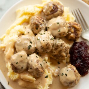 close up shot of Swedish meatballs on mashed potato on small white plate