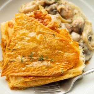 close up shot of chicken and mushroom pie garnished with fresh thyme in large white bowl