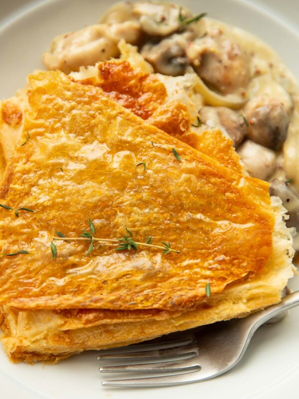 close up shot of chicken and mushroom pie garnished with fresh thyme in large white bowl