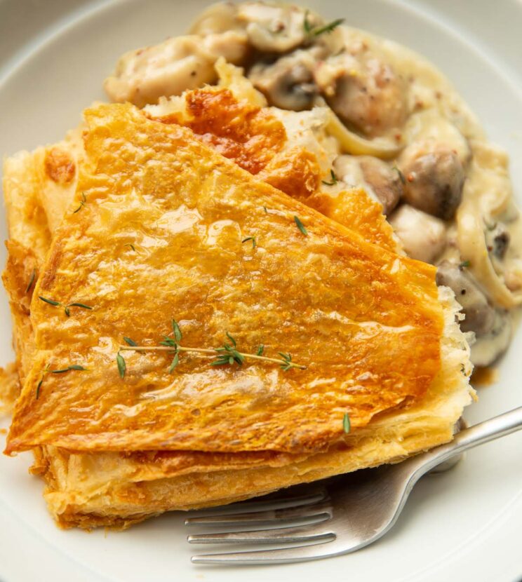 close up shot of chicken and mushroom pie garnished with fresh thyme in large white bowl