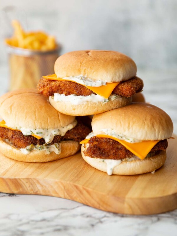 3 homemade filet-o-fish stacked on each other on wooden board with fries in the background