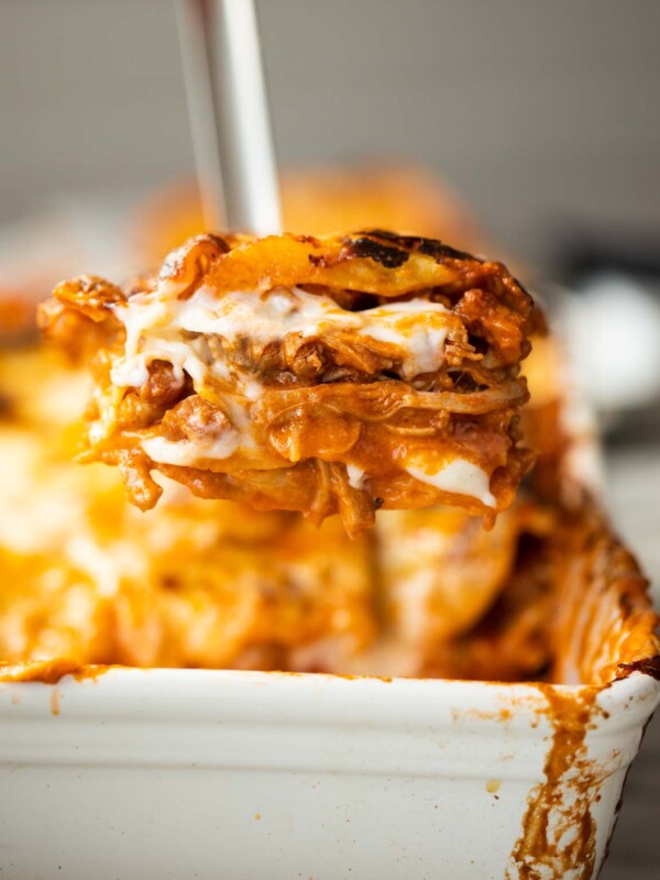 close up shot of metal spatula scooping chicken lasagne out of baking dish