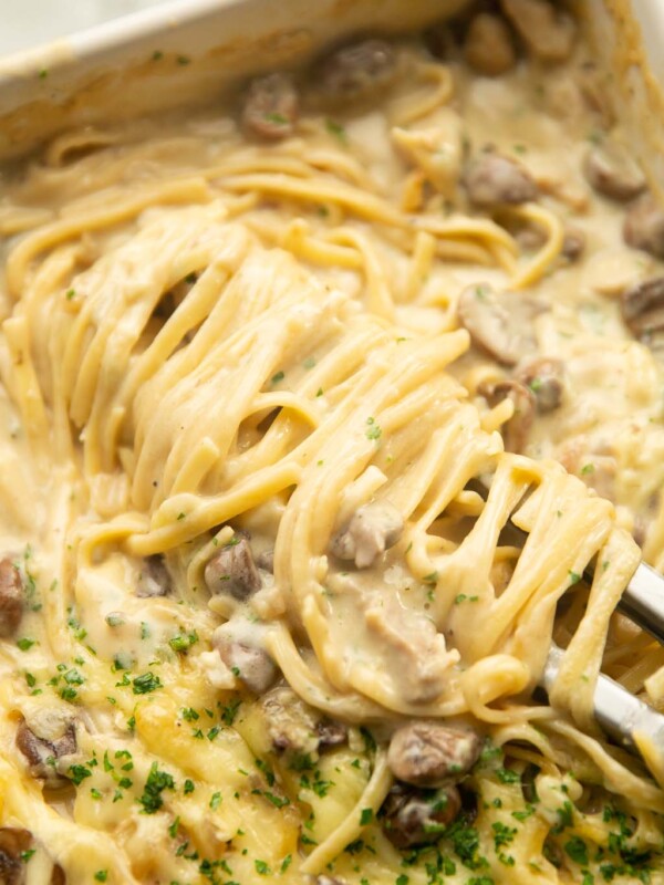 close up shot of pasta tongs twirling chicken tetrazzini in baking dish