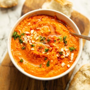 romesco sauce in large white bowl garnished with parsley smoked paprika and almonds