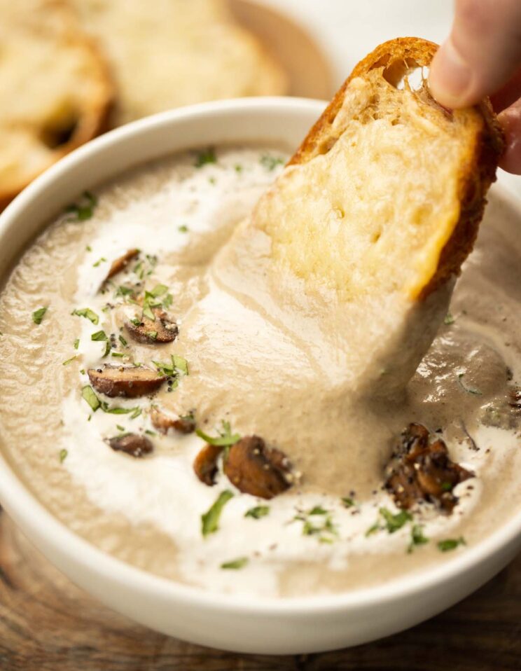 close up shot of hand dunking crostini into cream of mushroom soup