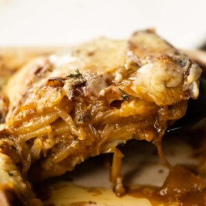 close up shot of spatula lifting french onion boulangere potatoes from baking dish