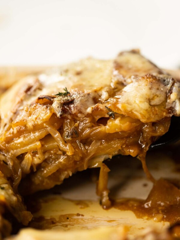 close up shot of spatula lifting french onion boulangere potatoes from baking dish