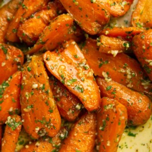 close up shot of garlic roasted carrots in large white baking dish