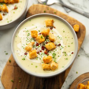 leek and potato soup served in small white bowl on wooden chopping board