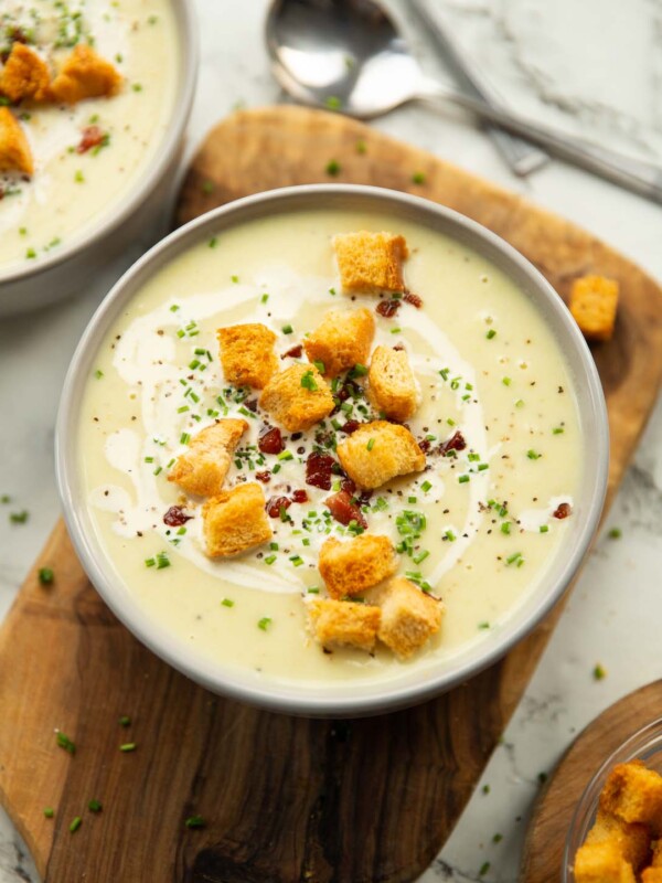 leek and potato soup served in small white bowl on wooden chopping board