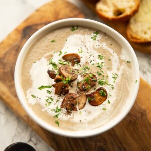 mushroom soup served in small white bowl on wooden chopping board with gruyere crostini