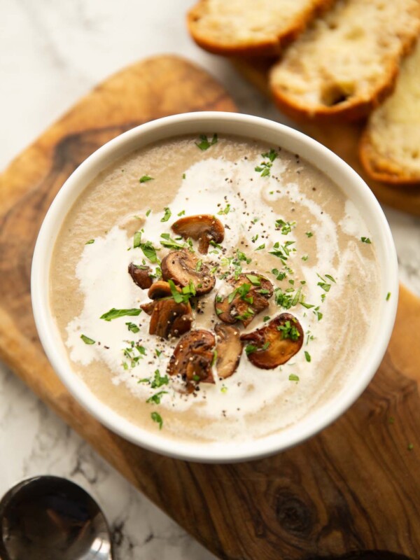 mushroom soup served in small white bowl on wooden chopping board with gruyere crostini